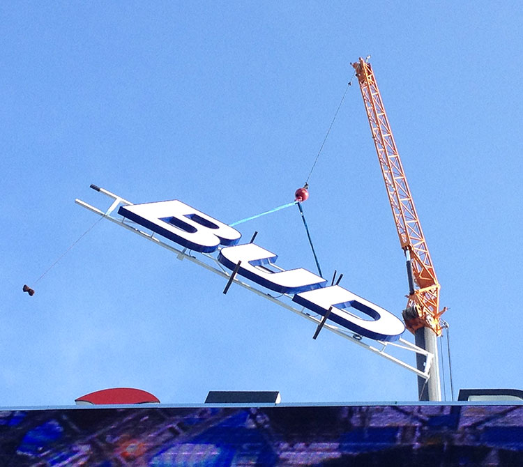 Bud light sign being installed on the top of a building by a Crain