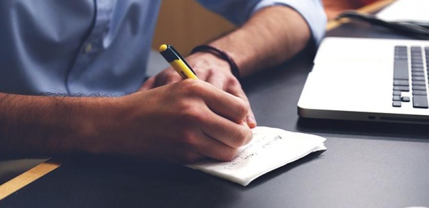 man taking notes with a yellow pen and paper